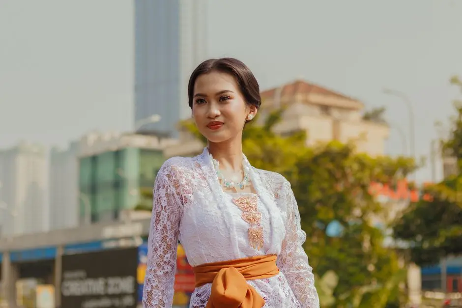 Seorang wanita Indonesia tengah merapikan outfit modern dengan paduan atasan putih dan celana panjang lebar di depan cermin